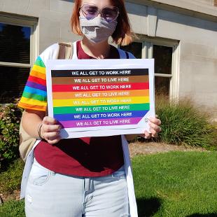 A student holding a rainbow flag sign that says 