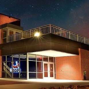 Full view of the Jim Herringa Athletic Center taken at night from west sideshowcasing the front and the entry way. The ornamental Hope Anchors on the exterior of the building and then entry way are lit up